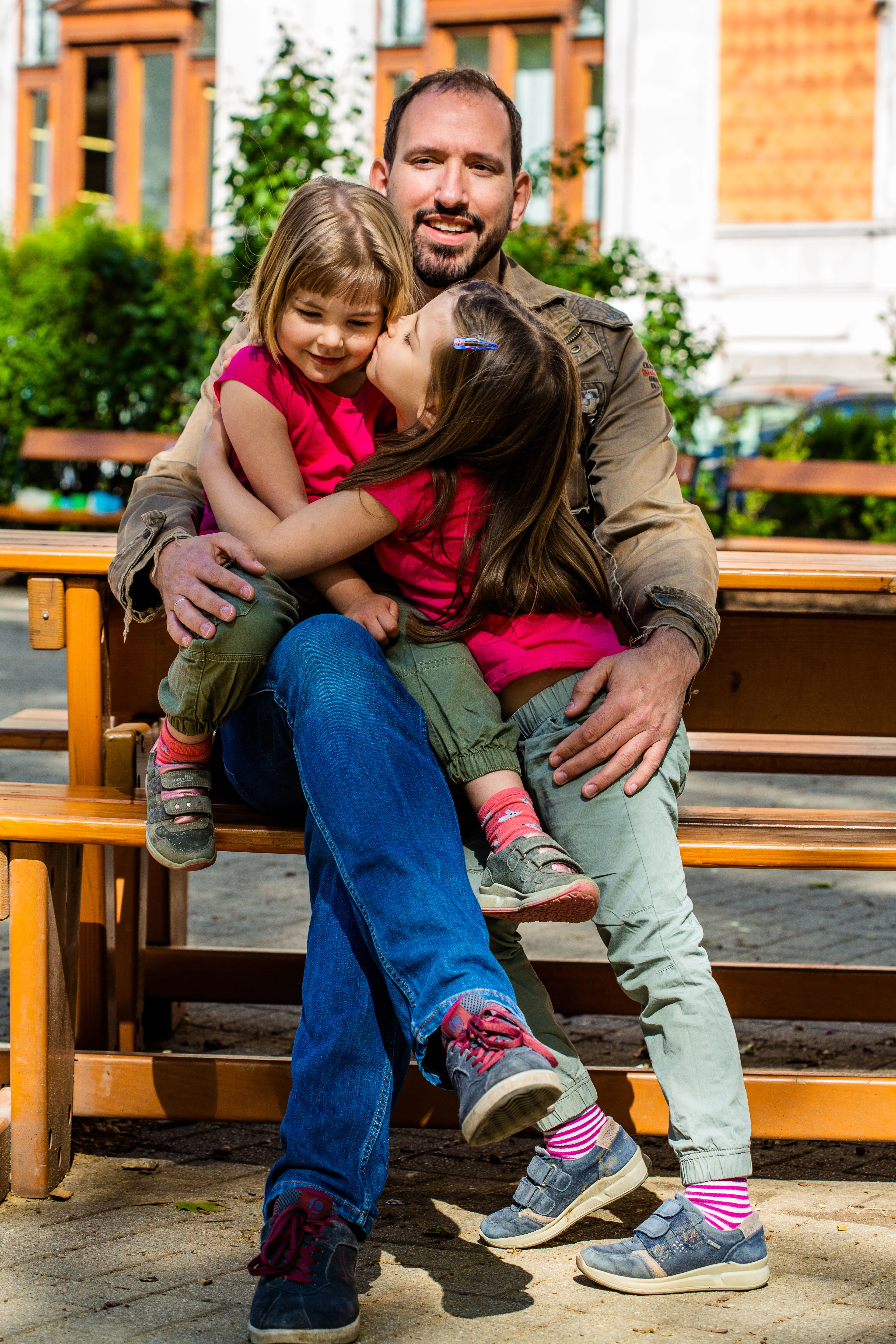 © Martin Marschall Papa umarmt seine beiden Kinder sitzend auf einer Parkbank